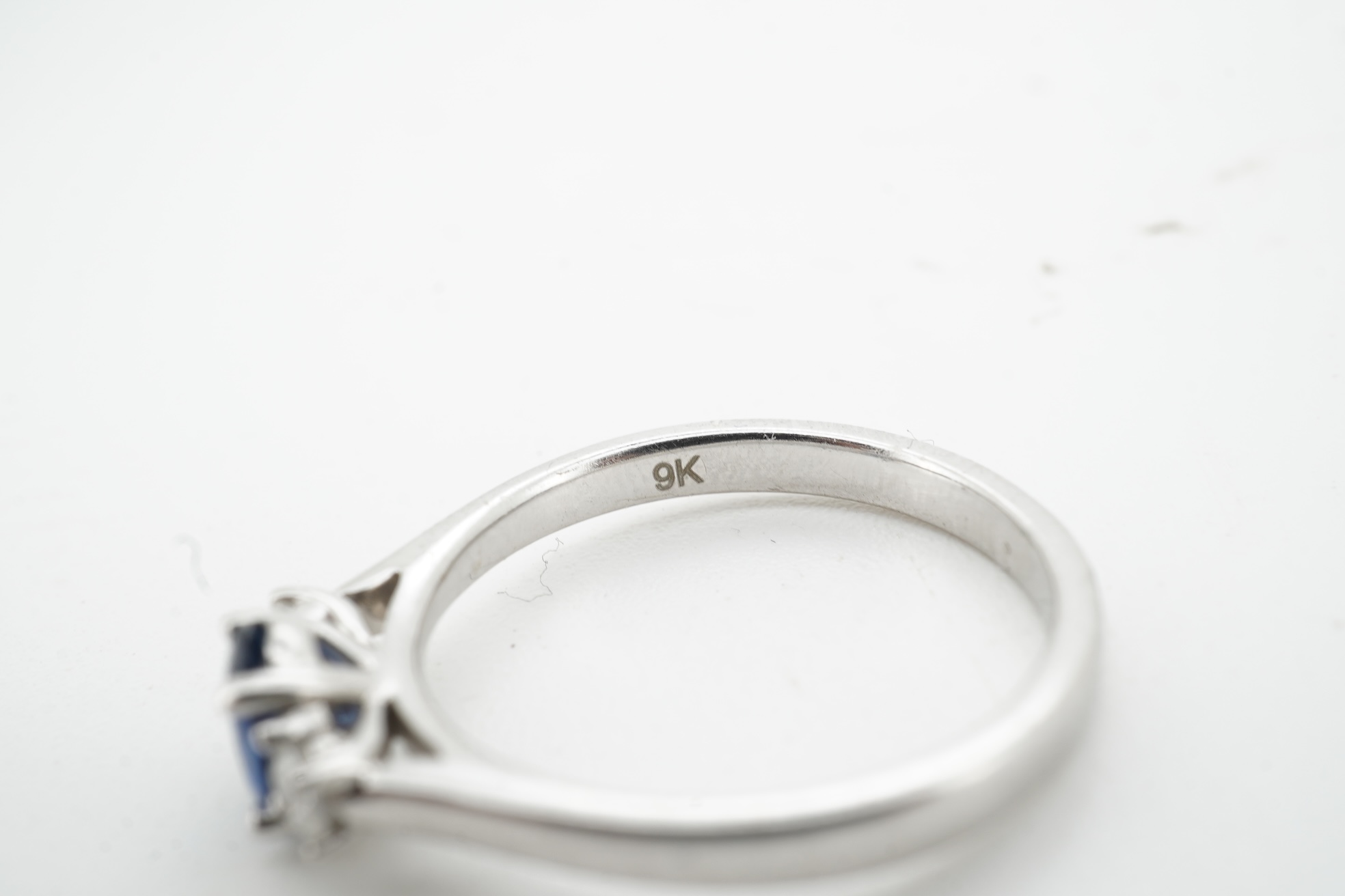 A sapphire and diamond three-stone ring, claw-set with an oval sapphire weighing approximately 0.35 carats, between shoulders set with brilliant-cut diamonds totalling approximately 0.12 carats, mounted in 9ct white gold